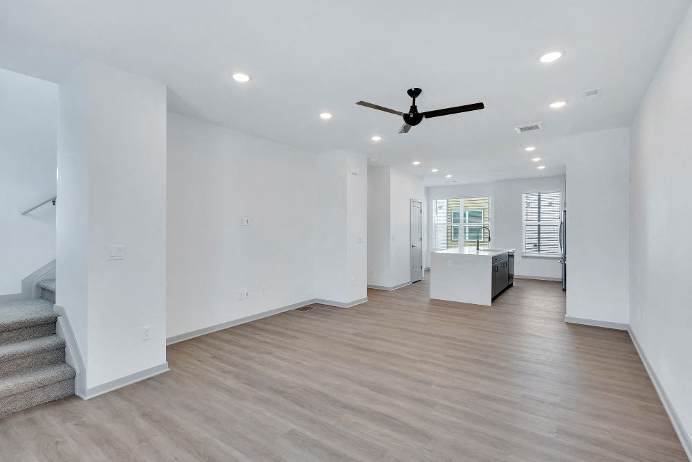 View of spacious living room with staircase on the left to the third floor, vinyl plank flooring, and the kitchen in the background